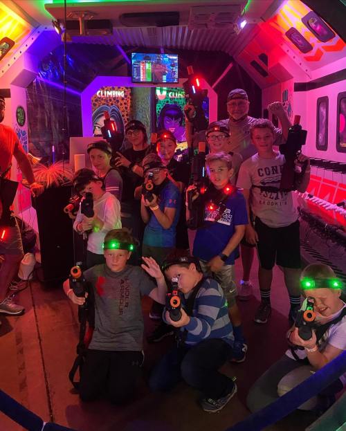 A group of kids in a neon-lit laser tag arena, posing with laser guns and wearing glowing headbands.