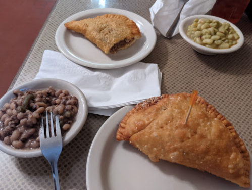 A plate with two golden empanadas, a side of black-eyed peas, and a bowl of green beans on a table.