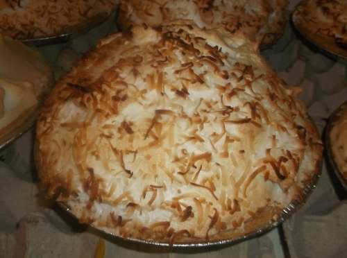A golden-brown coconut cream pie with a toasted meringue topping, displayed in a silver pie tin.