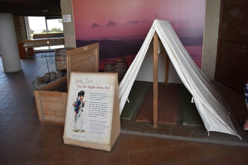 A white tent set up indoors next to a wooden display with an informational sign about the tent's history.