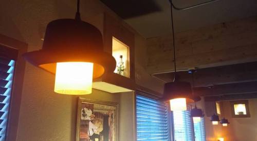 A cozy interior with pendant lights shaped like hats, wooden beams, and a small display nook with a bottle.