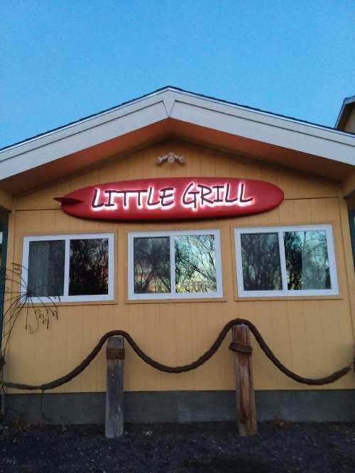 A yellow building with a sign reading "Little Grill" and large windows, featuring a surfboard design above the entrance.