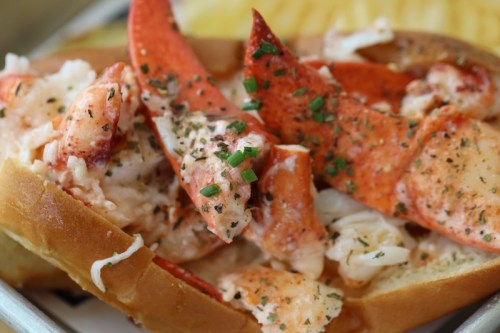 A close-up of a lobster roll topped with chives and seasoning, served on a toasted bun.