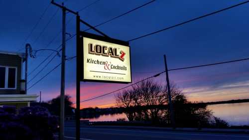 Sign for Local Z Kitchen & Cocktails at sunset, with a calm water view and colorful sky in the background.