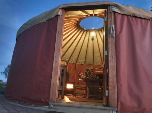 A cozy yurt interior with a wooden door open, revealing a warm, inviting space and a circular skylight above.