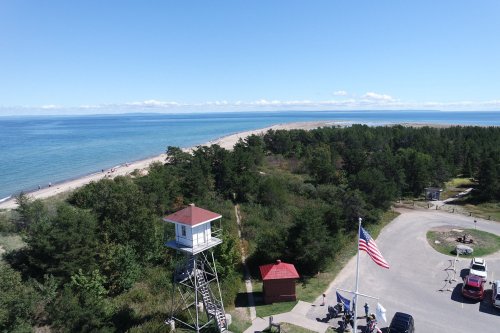 A scenic view of a beach with a lifeguard tower, trees, and a clear blue sky over the ocean.