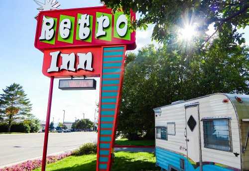 Colorful Retro Inn sign with a vintage trailer parked nearby, surrounded by greenery and sunlight.