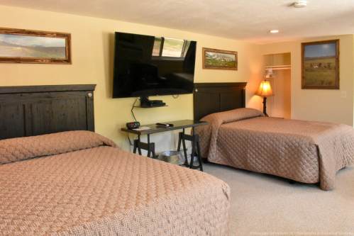 Cozy hotel room with two beds, a TV, a lamp, and framed artwork on the walls. Natural light from windows.