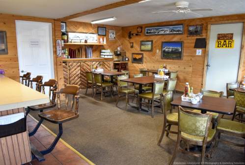 Cozy diner interior with wooden walls, tables set for dining, and a bar area in the background.