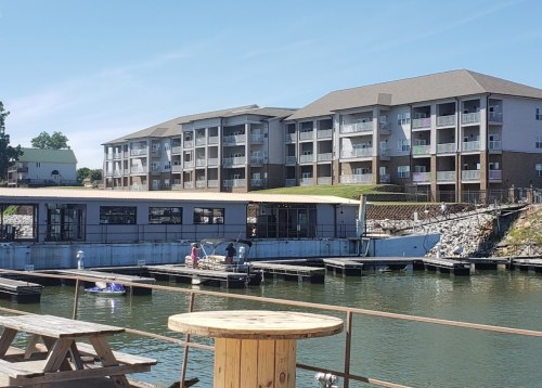 A marina with docks, a boat, and a multi-story building in the background under a clear blue sky.