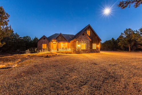 A cozy stone house illuminated at night, surrounded by trees under a bright moon.