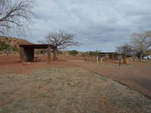 A park area with picnic shelters, bare trees, and a gravel path under a cloudy sky.