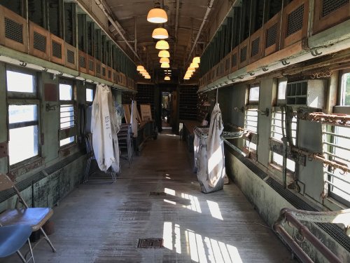 Interior of an old train car, featuring worn wooden floors, vintage lighting, and hanging white fabric.