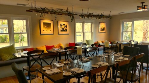 Cozy restaurant interior with wooden tables, colorful cushions, and framed artwork on the walls, illuminated by soft lighting.