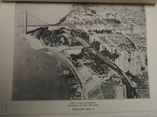 Aerial view of the New York approach to the Hudson River Bridge, showcasing roads and buildings along the riverbank.