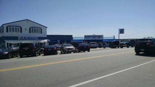A sunny day view of a street lined with parked cars and two businesses with blue awnings.