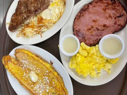 A tray with three plates: hash browns, eggs, ham, and French toast with butter and syrup.