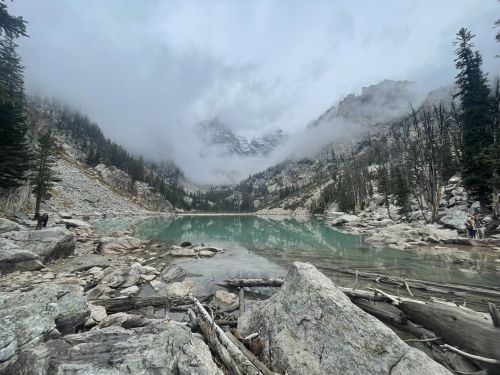 A serene lake surrounded by rocky terrain and misty mountains, with trees and fog creating a tranquil atmosphere.