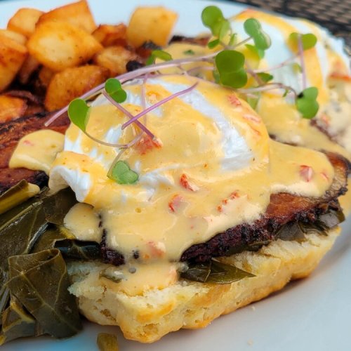A close-up of a dish featuring poached eggs on a biscuit, topped with hollandaise sauce and garnished with microgreens.