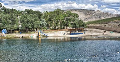 A serene lake surrounded by trees and mountains, featuring a slide and a shaded area for relaxation.