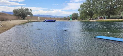 A serene lake with a blue inflatable float, surrounded by trees and mountains under a partly cloudy sky.