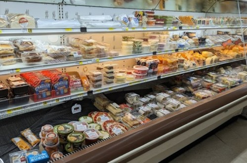 A grocery store deli case filled with various packaged meats, cheeses, and prepared foods.