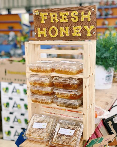 A wooden display stand with a sign reading "FRESH HONEY" and stacked containers of honey in clear packaging.