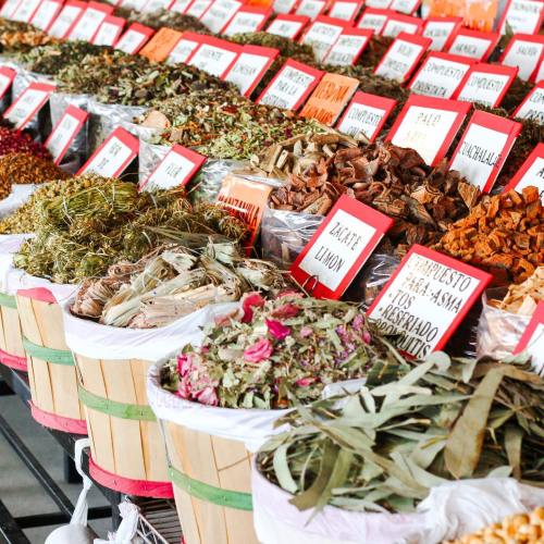 Colorful display of various dried herbs and spices in baskets, labeled with bright red signs at a market.
