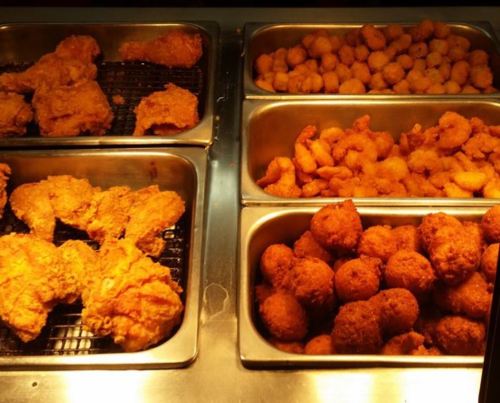 A display of fried chicken pieces, shrimp, and golden-brown hushpuppies in metal trays.