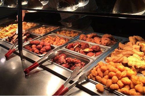 A buffet display featuring various fried foods, including chicken, tater tots, and fries, with serving tongs.
