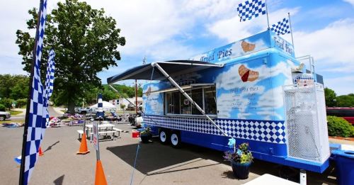A colorful food truck with a blue and white checkered design, serving fried pies, set up in a sunny outdoor area.