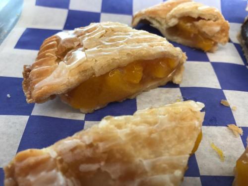 Close-up of flaky pastry with a golden fruit filling, resting on a blue and white checkered paper.