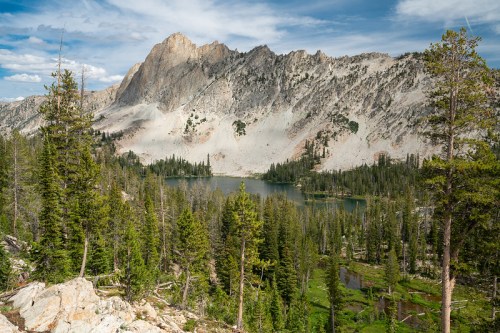 A scenic view of a mountain landscape with a lake surrounded by lush green trees and rocky peaks under a blue sky.