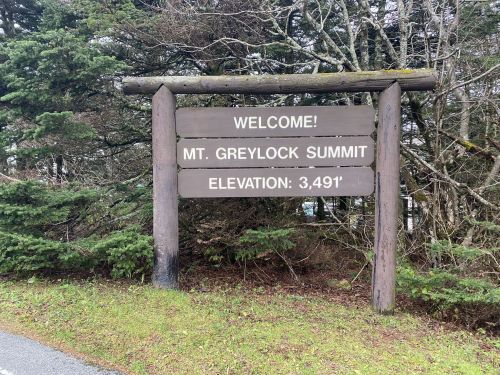 Welcome sign for Mt. Greylock Summit, elevation 3,491 feet, surrounded by trees.