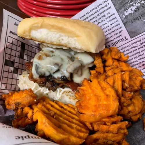 A delicious sandwich with melted cheese and toppings, served with crispy sweet potato fries on the side.