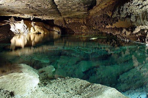A serene underground cave with clear water reflecting the rocky ceiling and walls, creating a tranquil atmosphere.