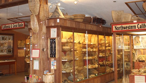 Display of woven baskets and artifacts in a museum showcasing California and Northwestern California cultures.