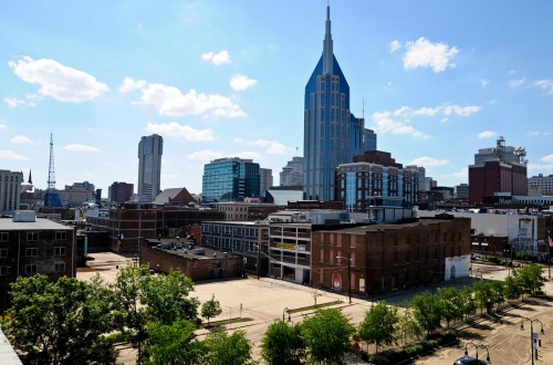 A city skyline featuring modern buildings and a prominent tall structure under a blue sky with scattered clouds.