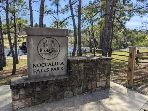 Sign for Noccalula Falls Park at Black Creek, surrounded by trees and a scenic landscape.