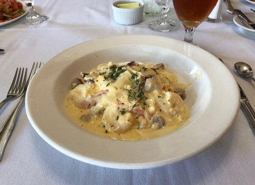 A creamy pasta dish with mushrooms and herbs, served in a white bowl on a table set with utensils.