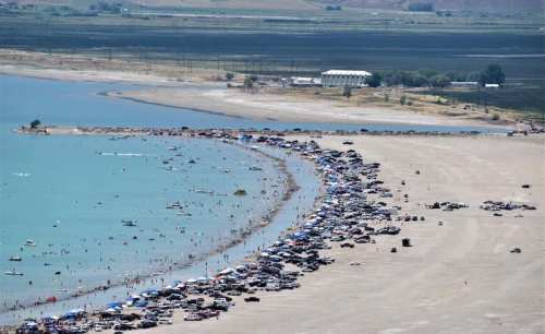 Aerial view of a crowded beach with cars parked along the shore and people enjoying the water on a sunny day.