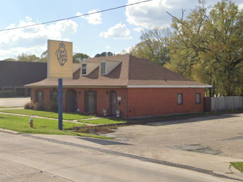 A brick building with a sloped roof and a sign reading "Not Just Pie," located on a street with green grass.