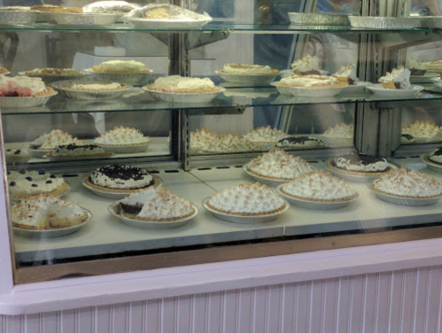 A display case filled with various pies topped with meringue and cream, showcasing a variety of flavors.