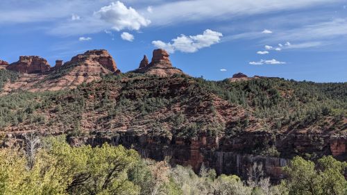 A scenic view of red rock formations and green trees under a blue sky with scattered clouds.