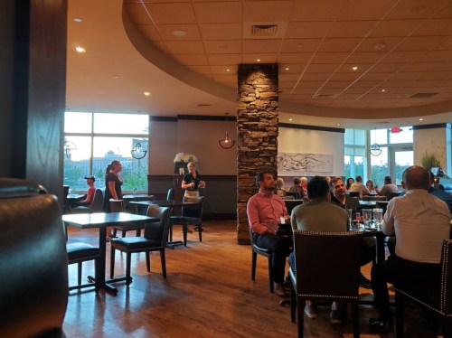 A restaurant interior with diners at tables, a stone column, and a server attending to guests in a lively atmosphere.