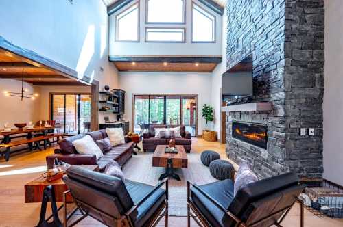 Spacious living room with high ceilings, large windows, stone fireplace, and modern furniture in a cozy setting.