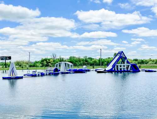 Inflatable water park with blue and white structures on a lake under a partly cloudy sky.