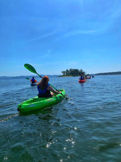 A group of people kayaking on a sunny day, with a small island in the background and clear blue skies.