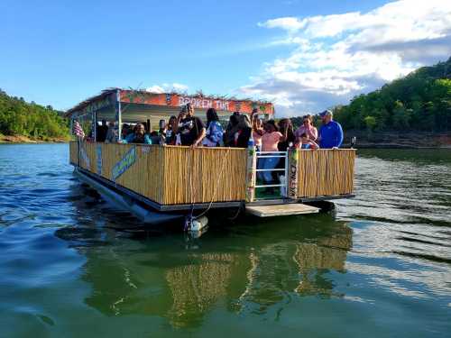 A group of people enjoying a party on a large boat on a lake, surrounded by trees and a blue sky.