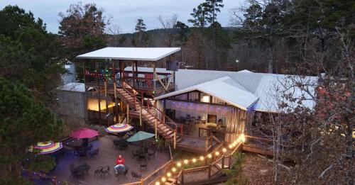 A rustic lodge with outdoor seating, colorful umbrellas, and festive lights, surrounded by trees in a serene setting.